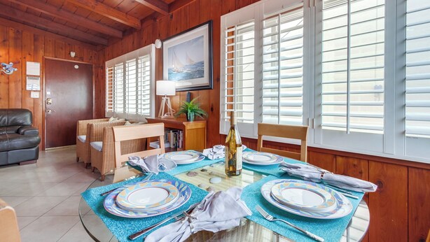 A dining area with a round table set for six, a bottle of wine, and a framed picture on the wall. - Have fun at the beach in this one bedroom cozy 1 bedroom apartment. (San Diego)