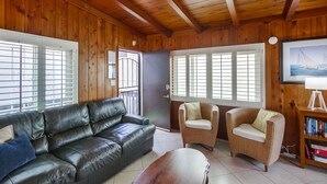 A wooden-paneled room with a leather sofa, two wicker chairs, a wooden coffee table, and a bookshelf. - Have fun at the beach in this one bedroom cozy 1 bedroom apartment. (San Diego)