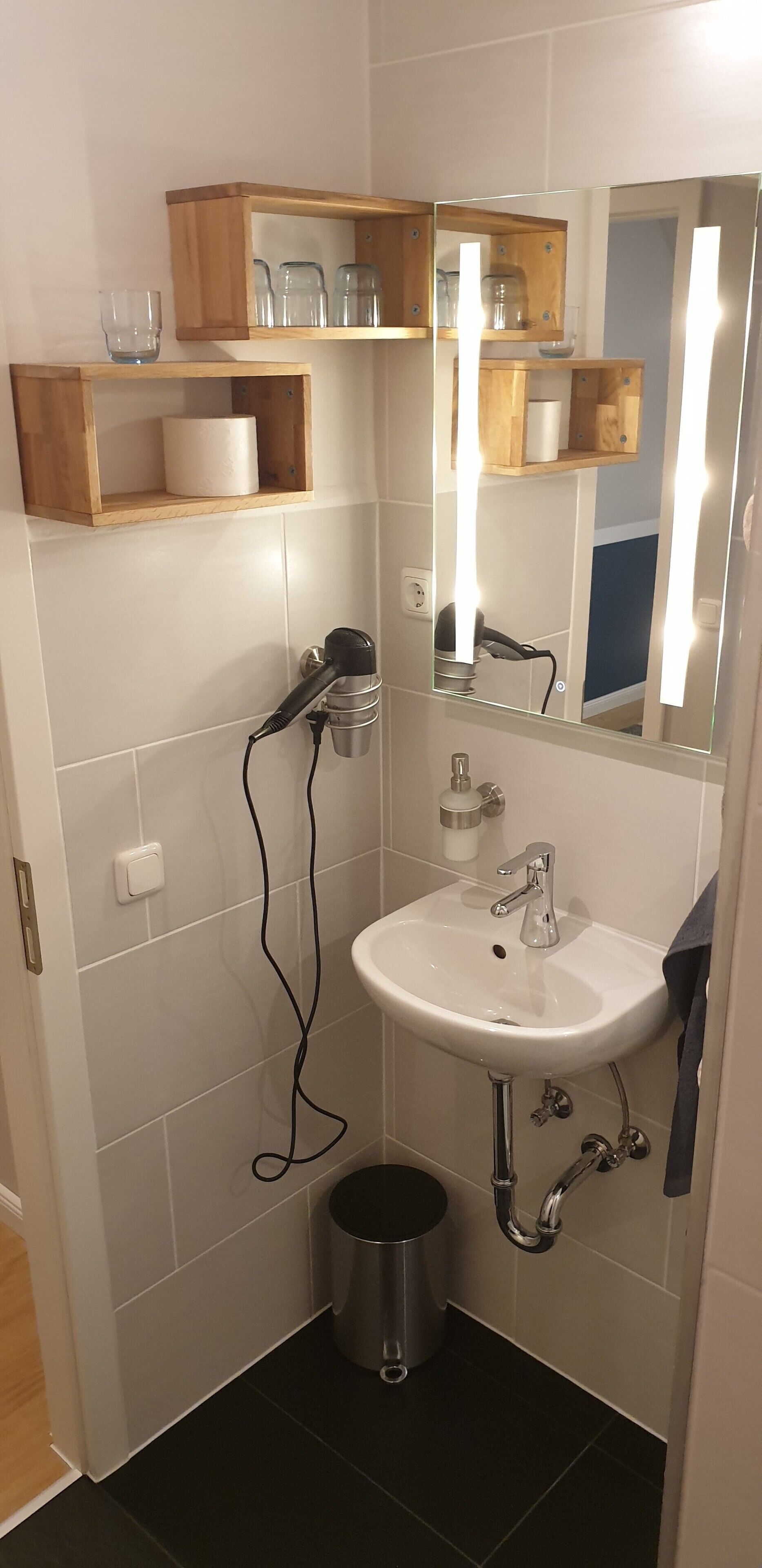 A compact bathroom with a white sink, a mirror, and a hairdryer on a wall-mounted shelf.
