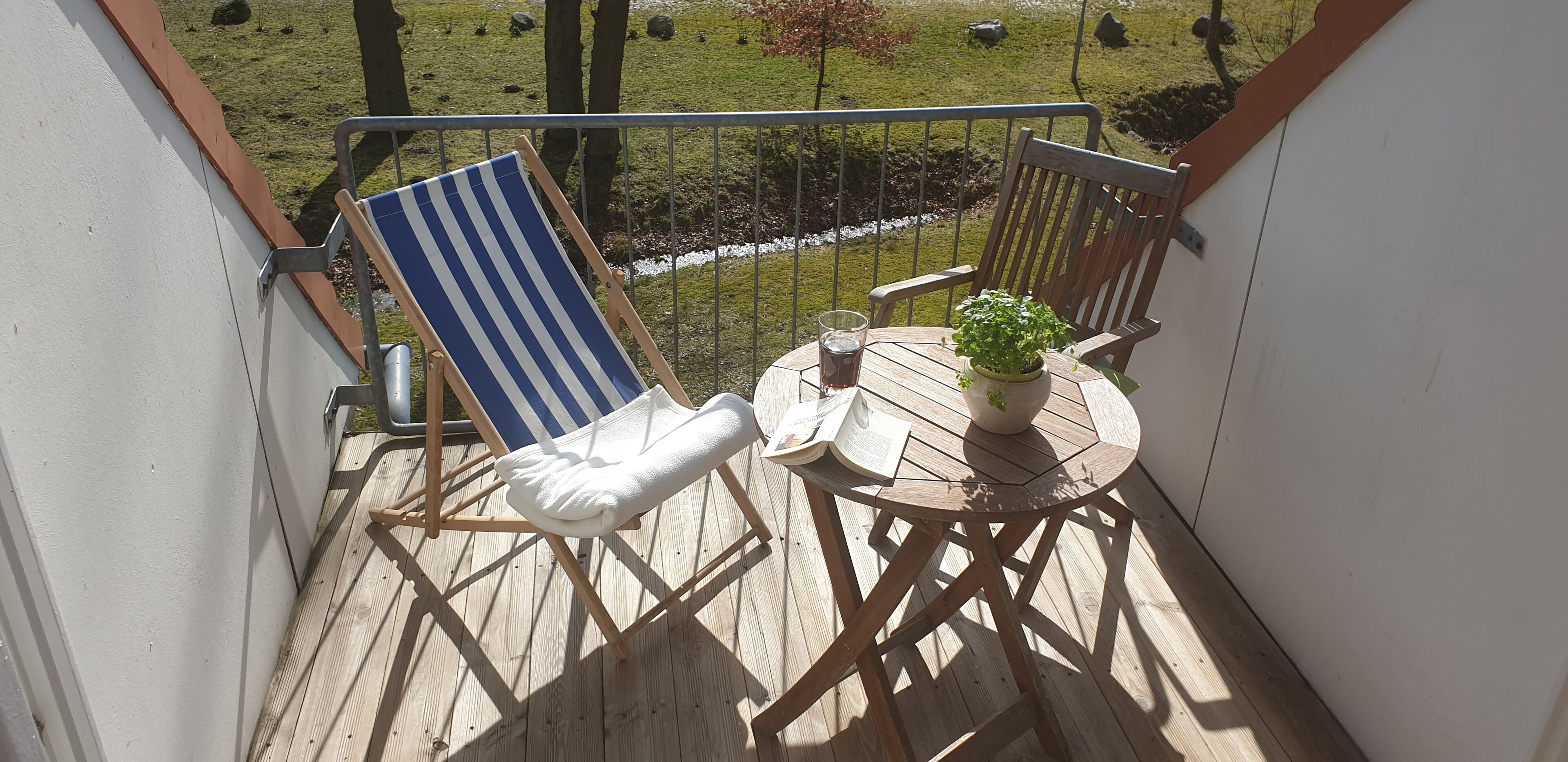 A balcony with a wooden chair, a small round table, and a potted plant.