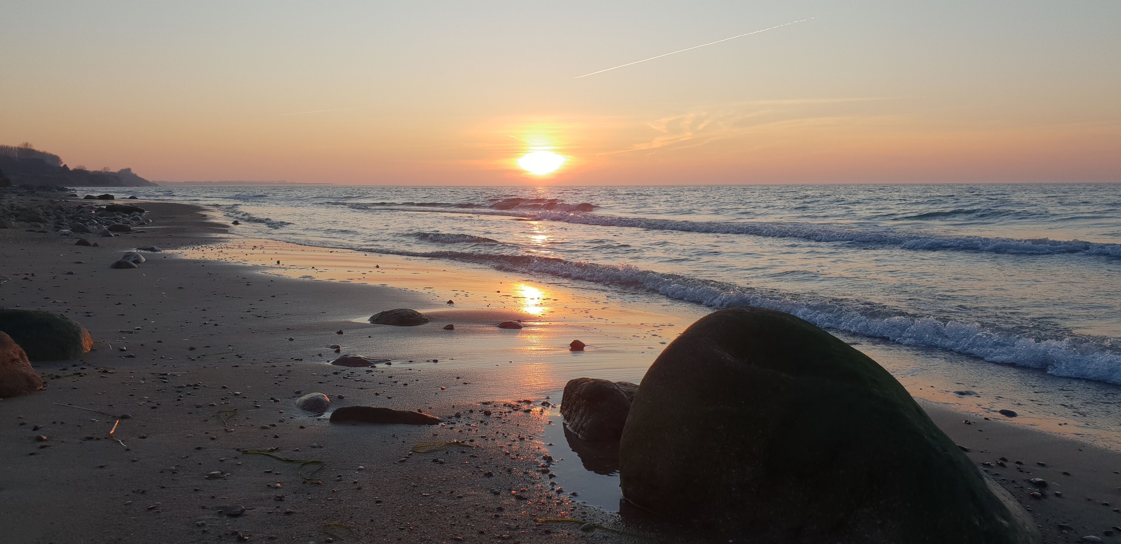 A beach with rocks and waves at sunset.