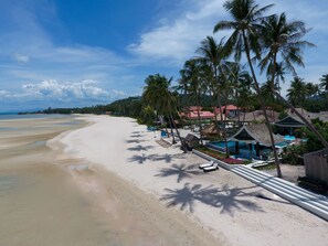Un complejo turístico en la playa con una orilla de arena, palmeras y una zona de piscina.