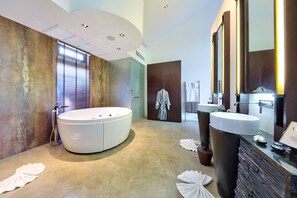 A modern bathroom with a large bathtub, two sinks, and a large mirror.