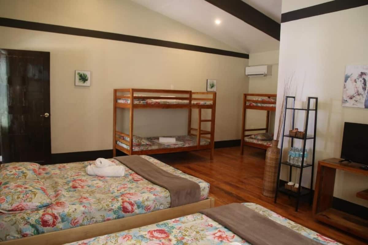 A room with two wooden bunk beds, a television, a shelf with bottles, and a door.