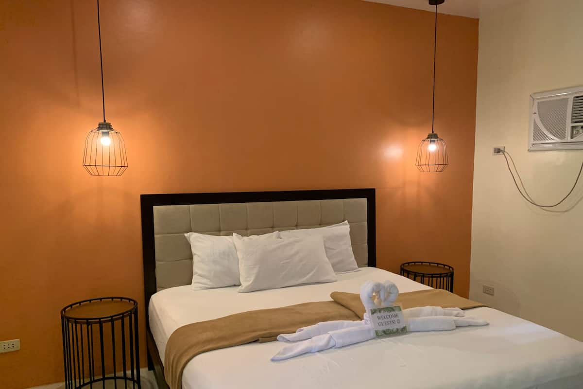 A hotel room with a bed, two bedside tables, a wall-mounted air conditioner, and two pendant lights.