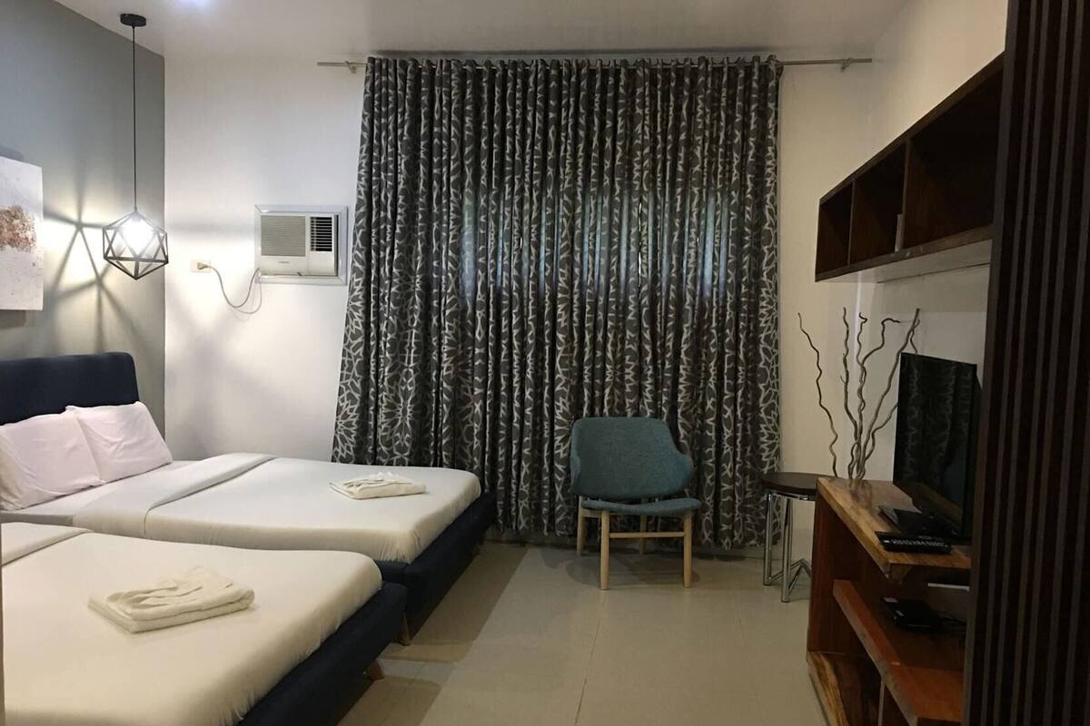 A hotel room with two beds, a chair, a TV, and a curtain.