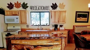 A kitchen with wooden cabinets, a microwave, a stove, a sink, and a wooden island with a 'WELCOME' sign above. - Mountain Views and Great Fire Pit (Star Valley)
