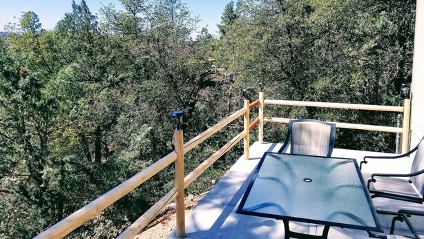 A balcony with a glass table and chairs, surrounded by a wooden railing, overlooking a dense forest. - Mountain Views and Great Fire Pit (Star Valley)