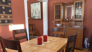 Un coin repas comprenant une table en bois, quatre chaises, deux bougies rouges, un buffet en bois et un miroir.
