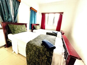 Een hotelkamer met twee bedden, een houten hoofdeinde, een raam met gordijnen en een betegelde vloer.