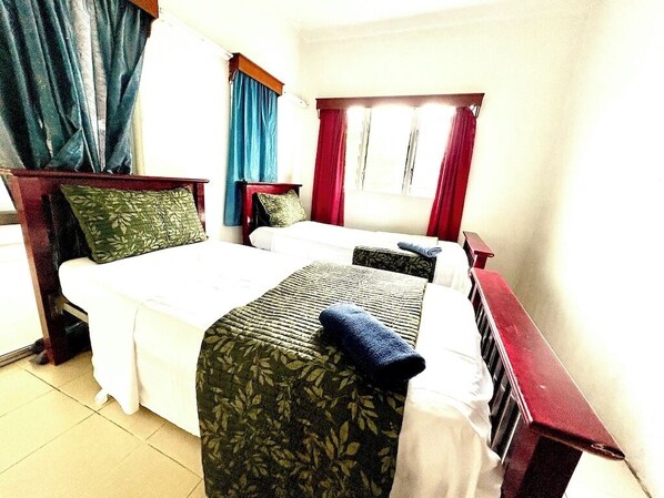 Een hotelkamer met twee bedden, een houten hoofdeinde, een raam met gordijnen en een betegelde vloer.