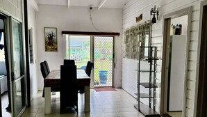 Ruime kamer met een eettafel en stoelen, een groot raam en een deur met een metalen hekwerk.