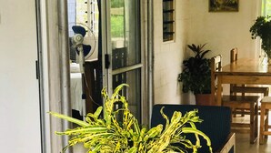 Een kamer met een ronde tafel, twee stoelen, een vaas met groene planten, een schilderij aan de muur en een raam met gordijnen.