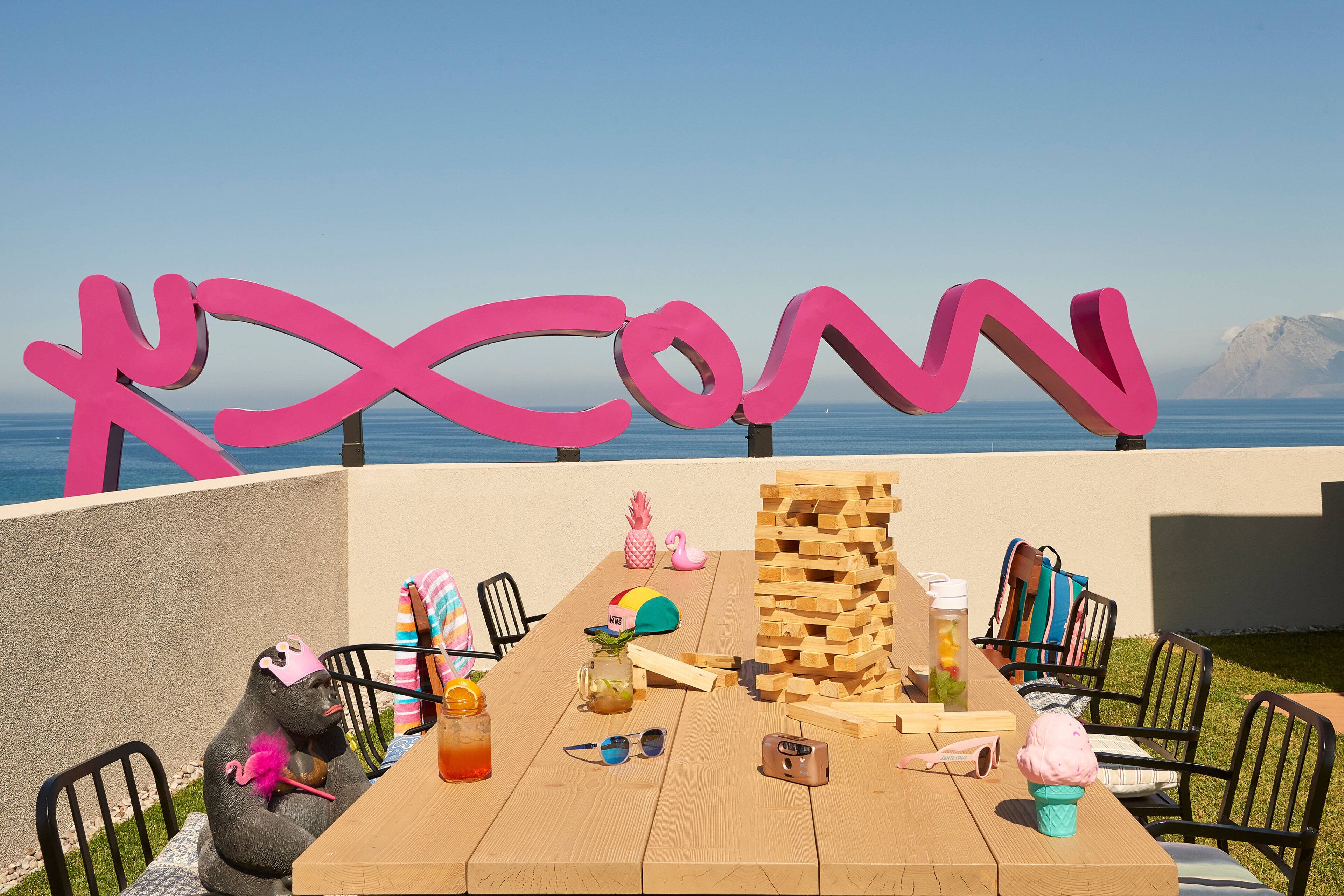 Una mesa de madera con varios objetos, entre ellos una pila de bloques de madera, una piña, un flamenco rosa y un cono de helado rosa.