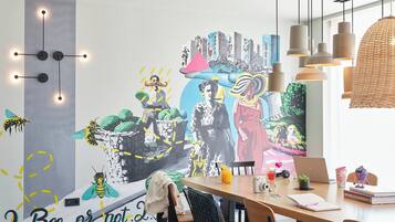 Un comedor con un mural, una mesa con sillas, una computadora portátil y varios objetos sobre la mesa.