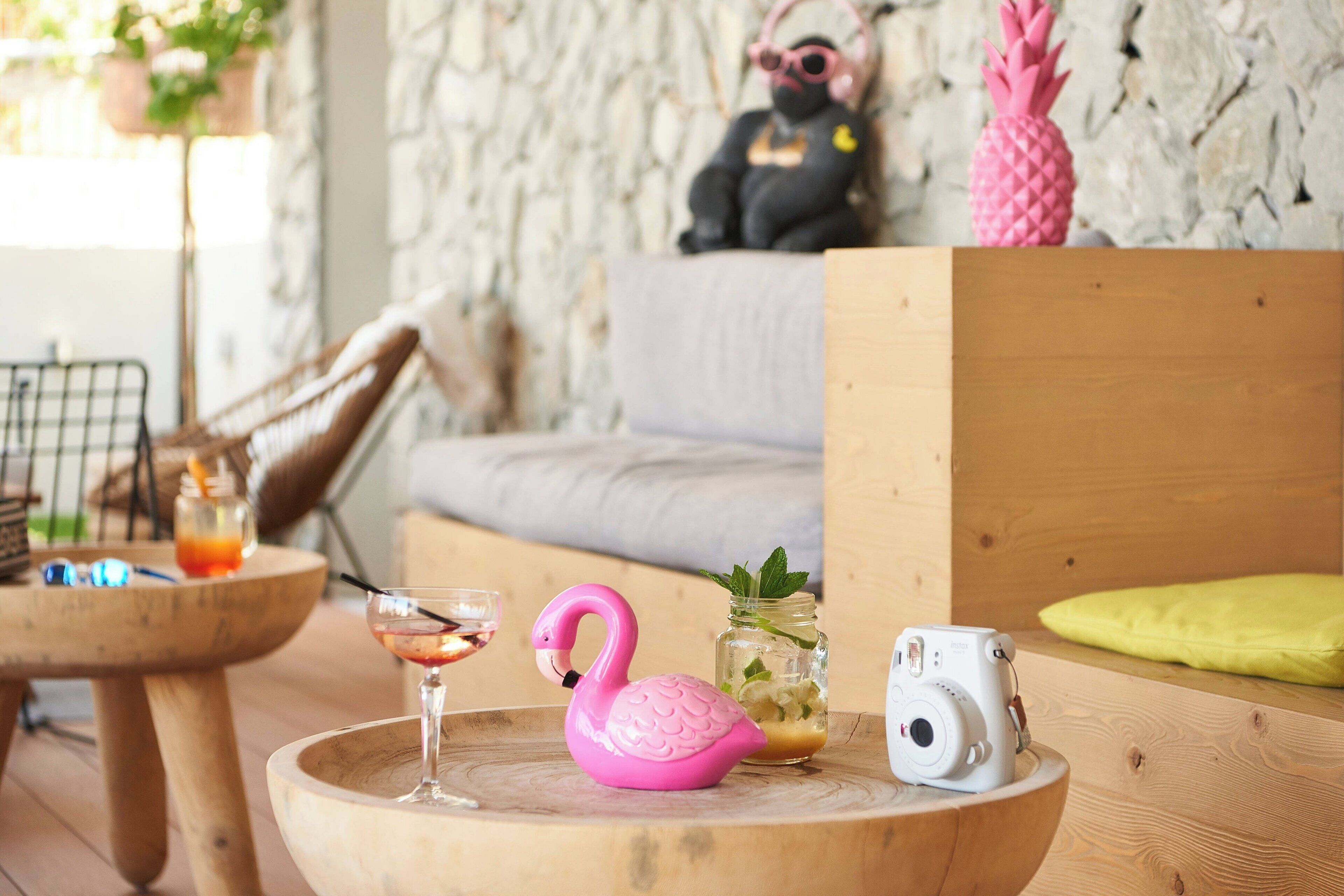 A cozy room with a wooden table, a pink flamingo figurine, a camera, and a mason jar with mint leaves.