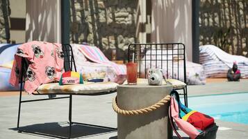 A poolside area with a chair covered in a pink blanket, a drink on a table, and a bag hanging on a rope.