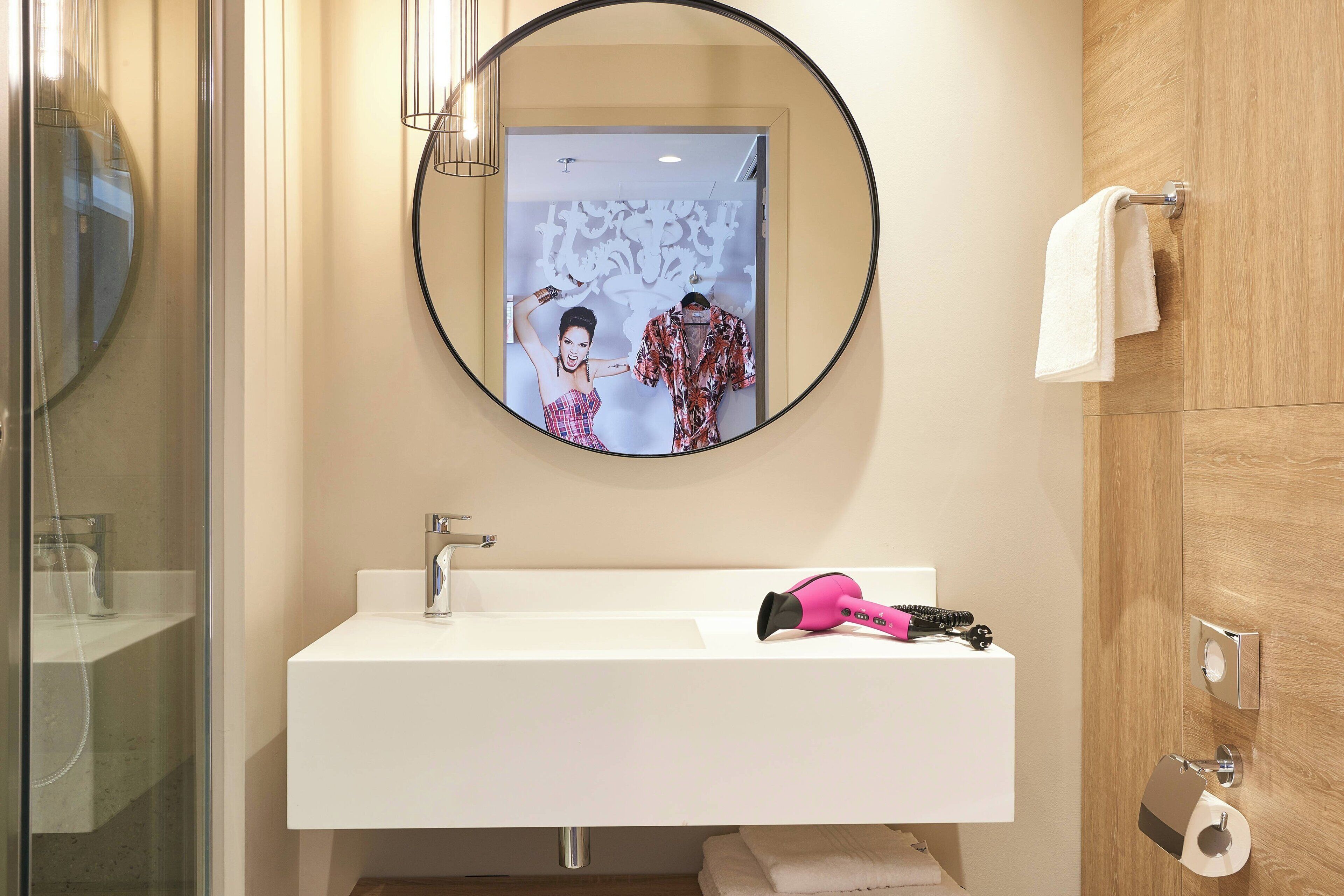 A modern bathroom with a white sink, a round mirror, and a towel rack.