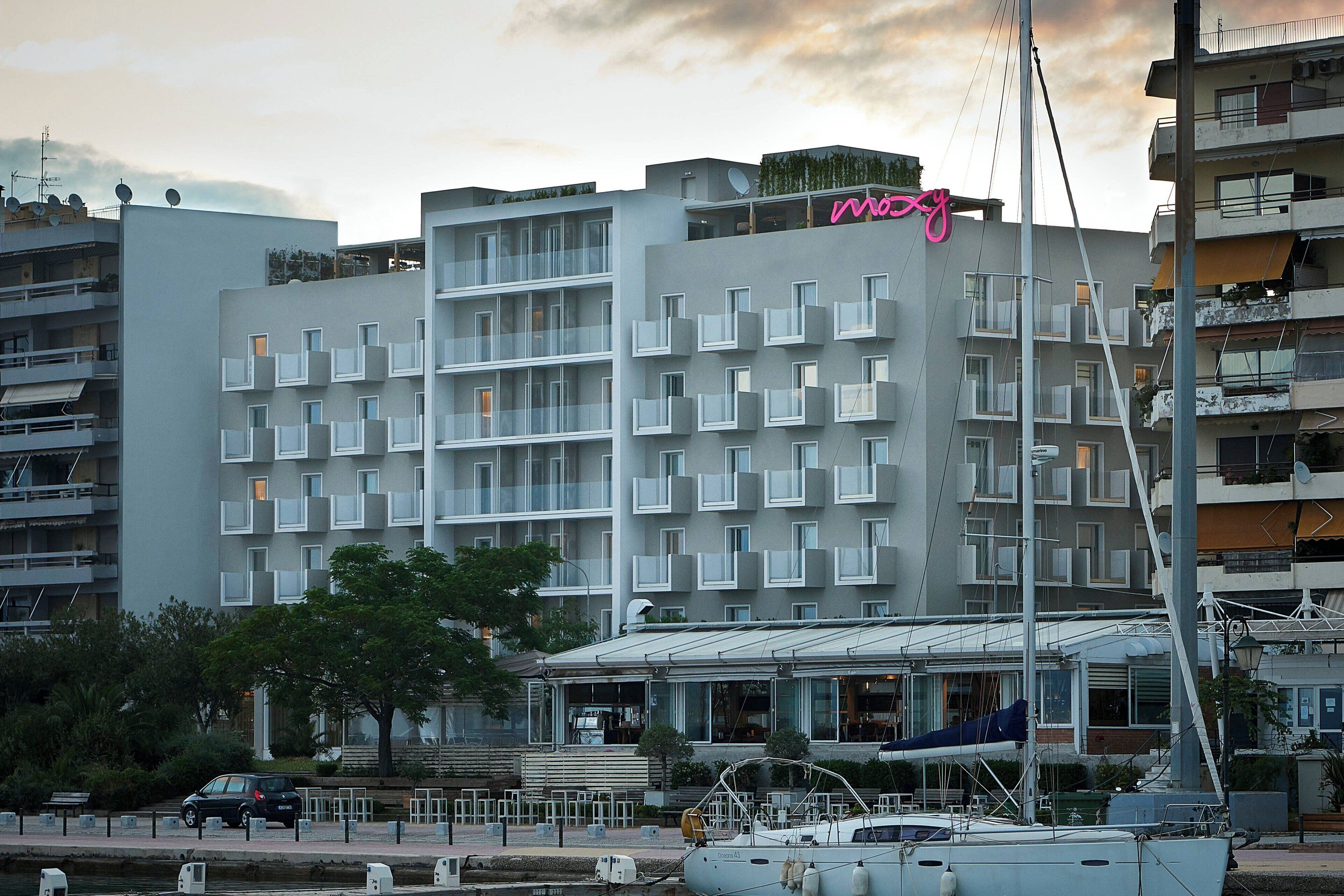 Un hotel moderno con varios balcones, un jardín en la azotea y un letrero de neón.