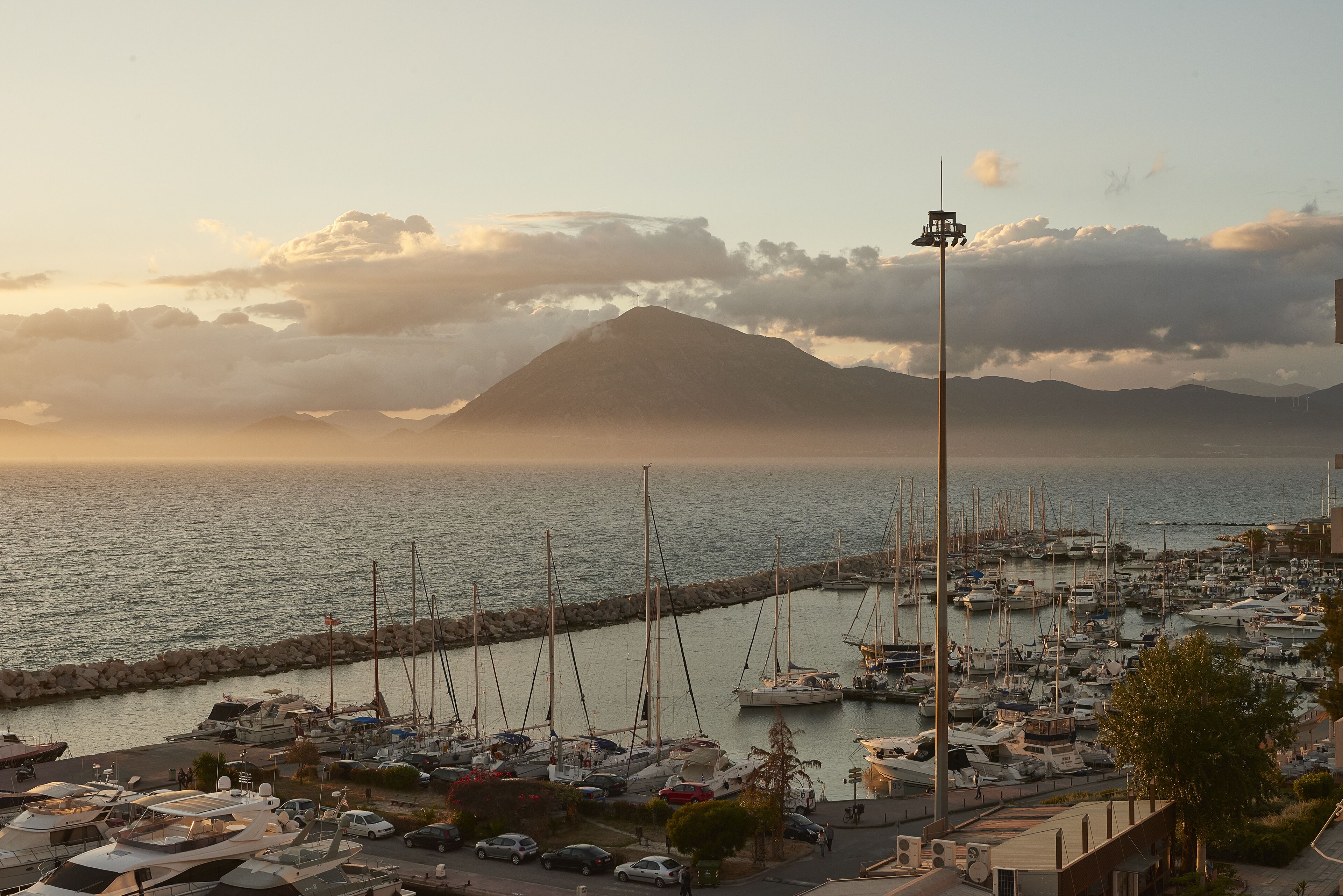 A marina with boats docked, a rocky breakwater, and a mountain in the background.