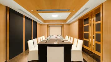 A conference room with a long table, white chairs, and a projector screen at the front.