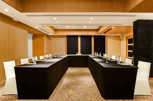 Un salón de conferencias con una larga mesa, sillas blancas y botellas de agua sobre la mesa.