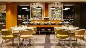 A restaurant with a bar area, multiple tables with chairs, and a variety of bottles and jars on display. - Lemon Tree Hotel Viman Nagar Pune (Pune)