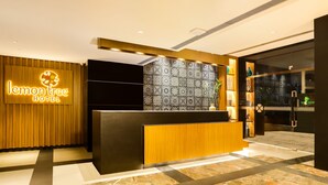 A hotel reception area with a modern design, featuring a wooden reception desk, a patterned wall, and a well-lit interior. - Lemon Tree Hotel Viman Nagar Pune (Pune)