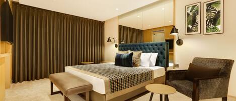 A modern hotel room with a large bed, a bench, a chair, a small table, and a large mirror.