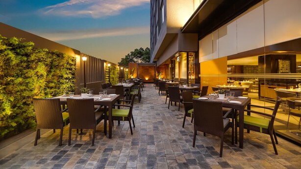 An outdoor dining area with tables and chairs, a stone floor, and a view of the sky. - Lemon Tree Hotel Viman Nagar Pune (Pune)