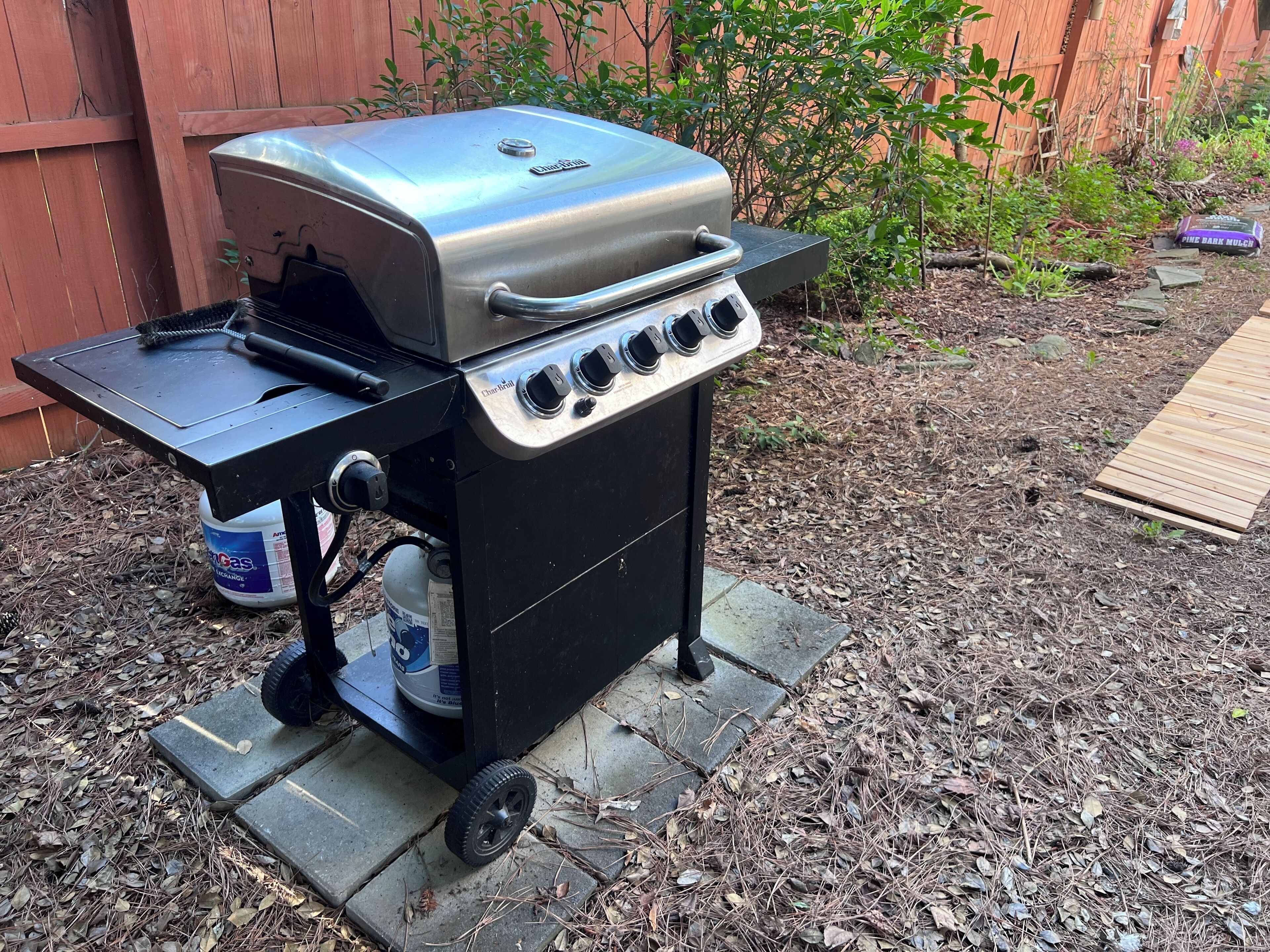 Ein tragbarer Grill mit Gasflasche und Metalldeckel, platziert auf einer Steinfläche im Freien.