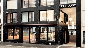 Un edificio moderno con un llamativo letrero 'ART HOUSE', ventanas amplias y una entrada visible con una línea roja sobre la puerta.