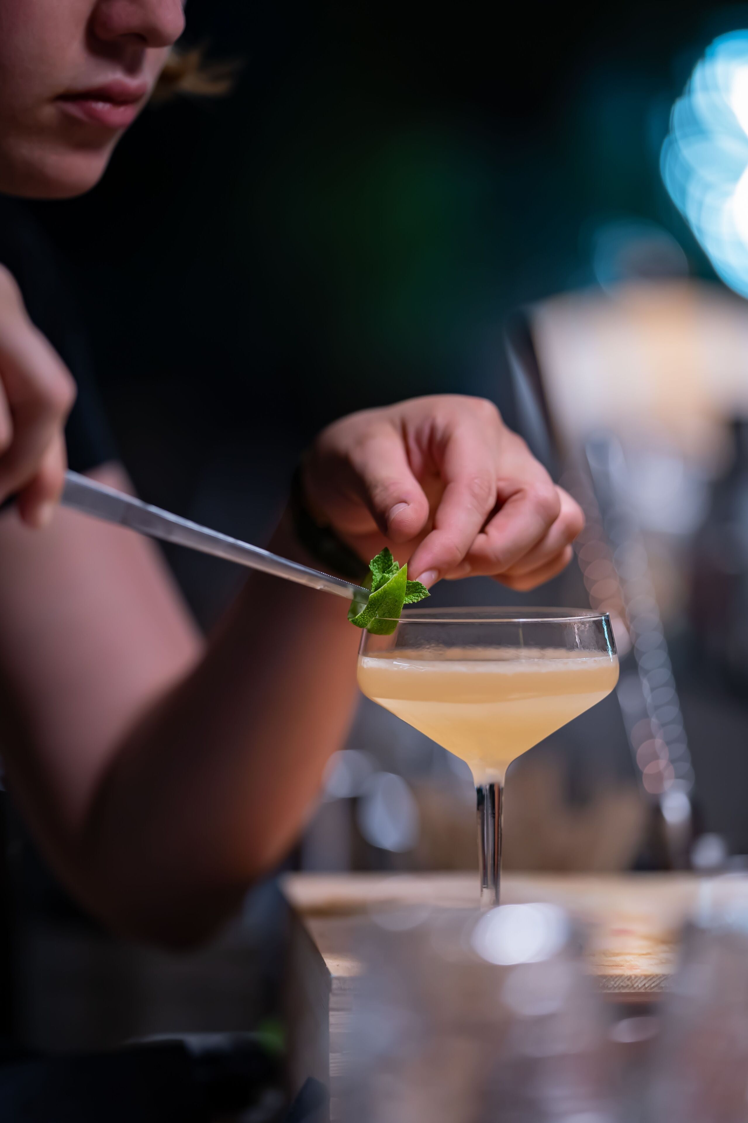 A person using a knife to garnish a cocktail with a mint leaf.