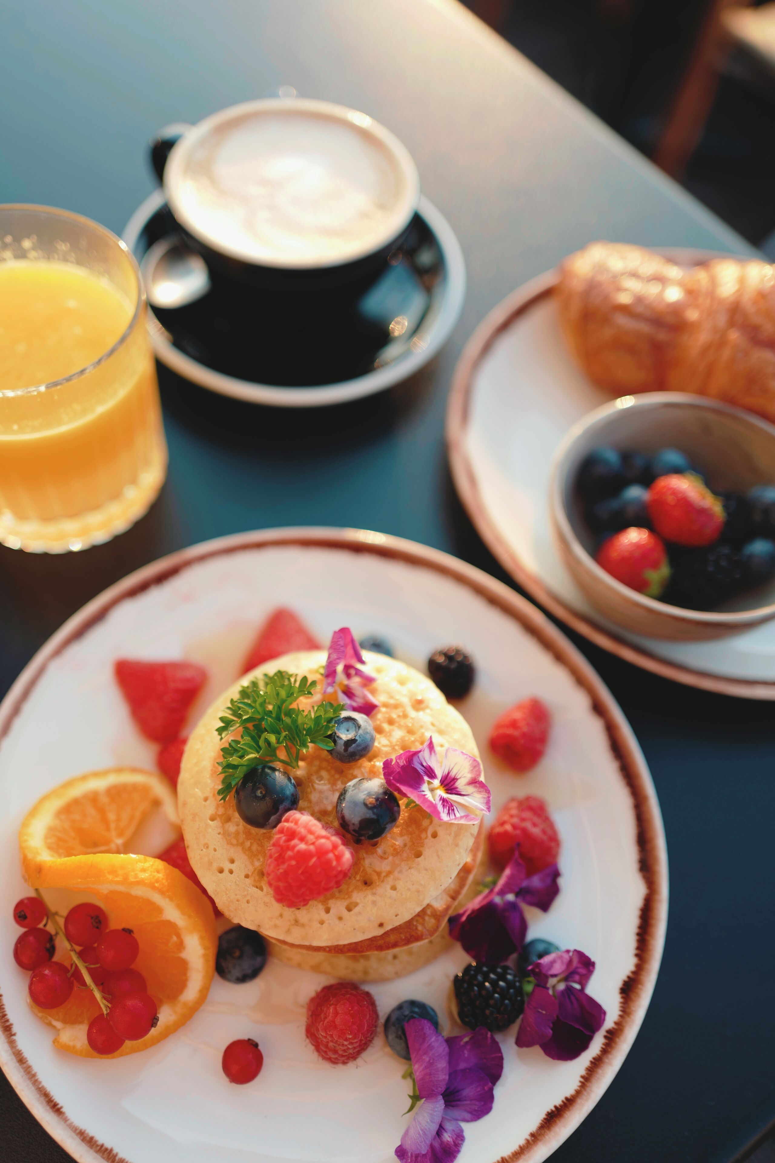 A breakfast setting with pancakes, coffee, croissant, and a bowl of berries.