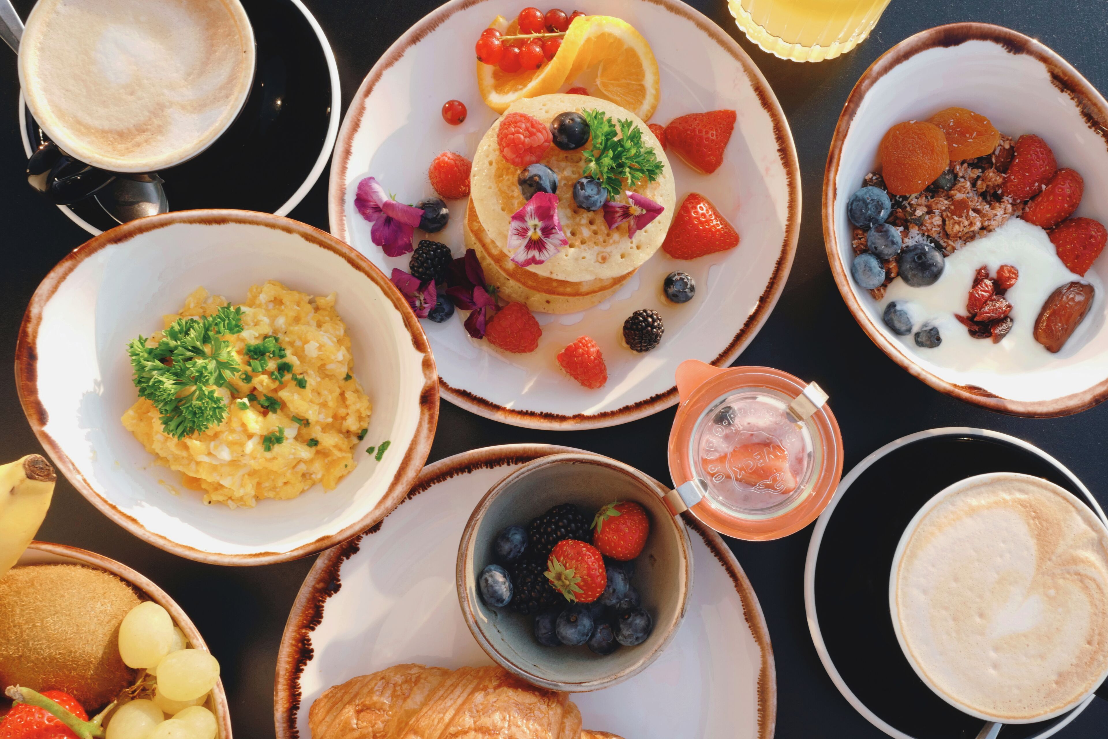 Uma mesa de café da manhã com diversos pratos, incluindo panquecas, ovos mexidos e frutas frescas.