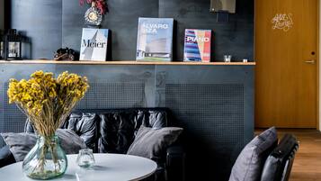 A modern reception area with a black leather couch, a round table with a vase of yellow flowers, and a wooden reception desk displaying books and a decorative clock.