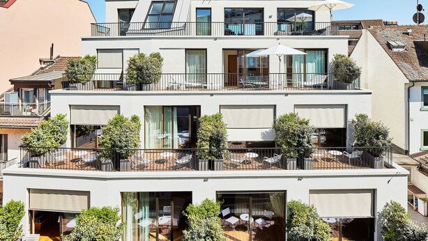 Un edificio de varios pisos con balcones, mobiliario exterior y grandes ventanales.