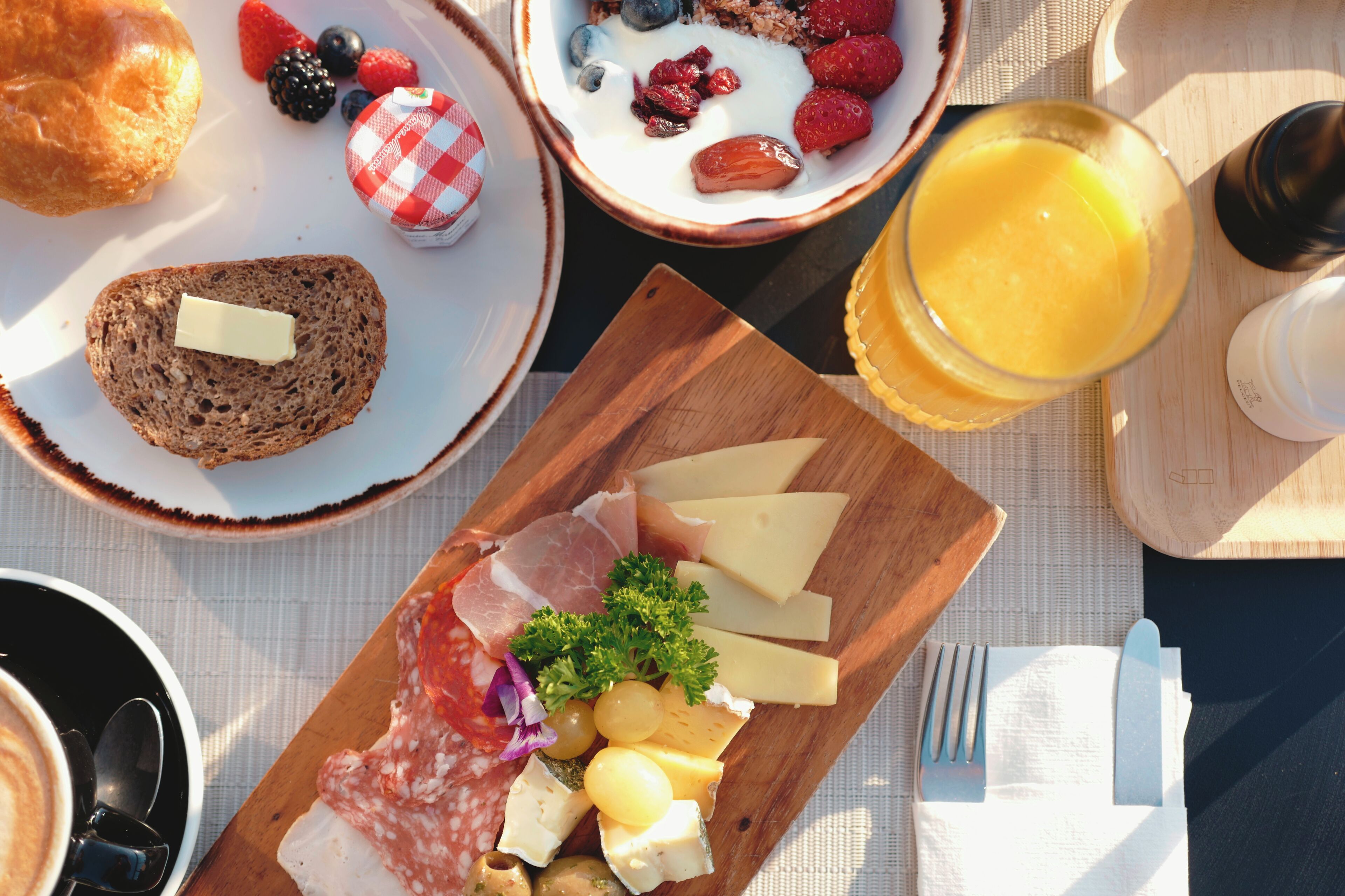 A breakfast setting with bread, cheese, fruits, and a glass of orange juice on a table.