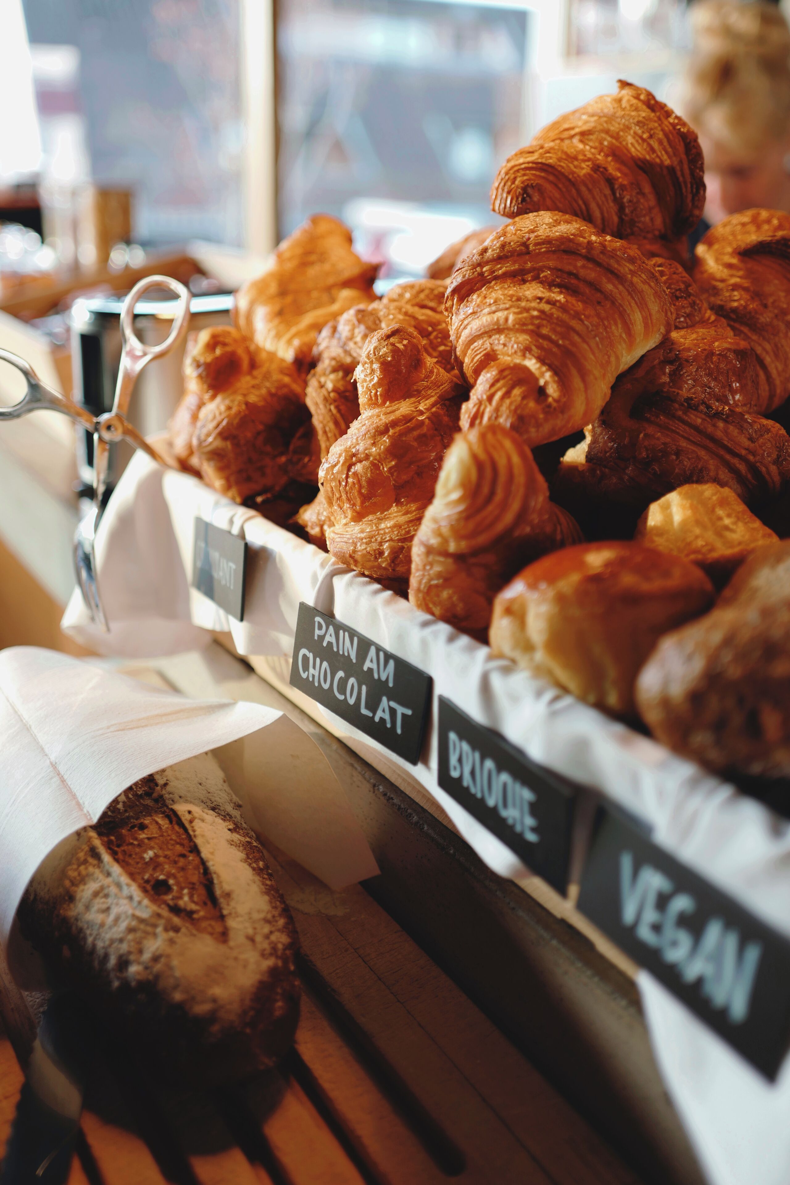 A display of various pastries, including croissants and pain au chocolat, with labels indicating options like vegan.