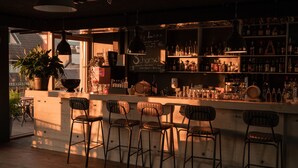 Zona de bar con taburetes de madera, diversas botellas de licores y una pizarra con la carta.