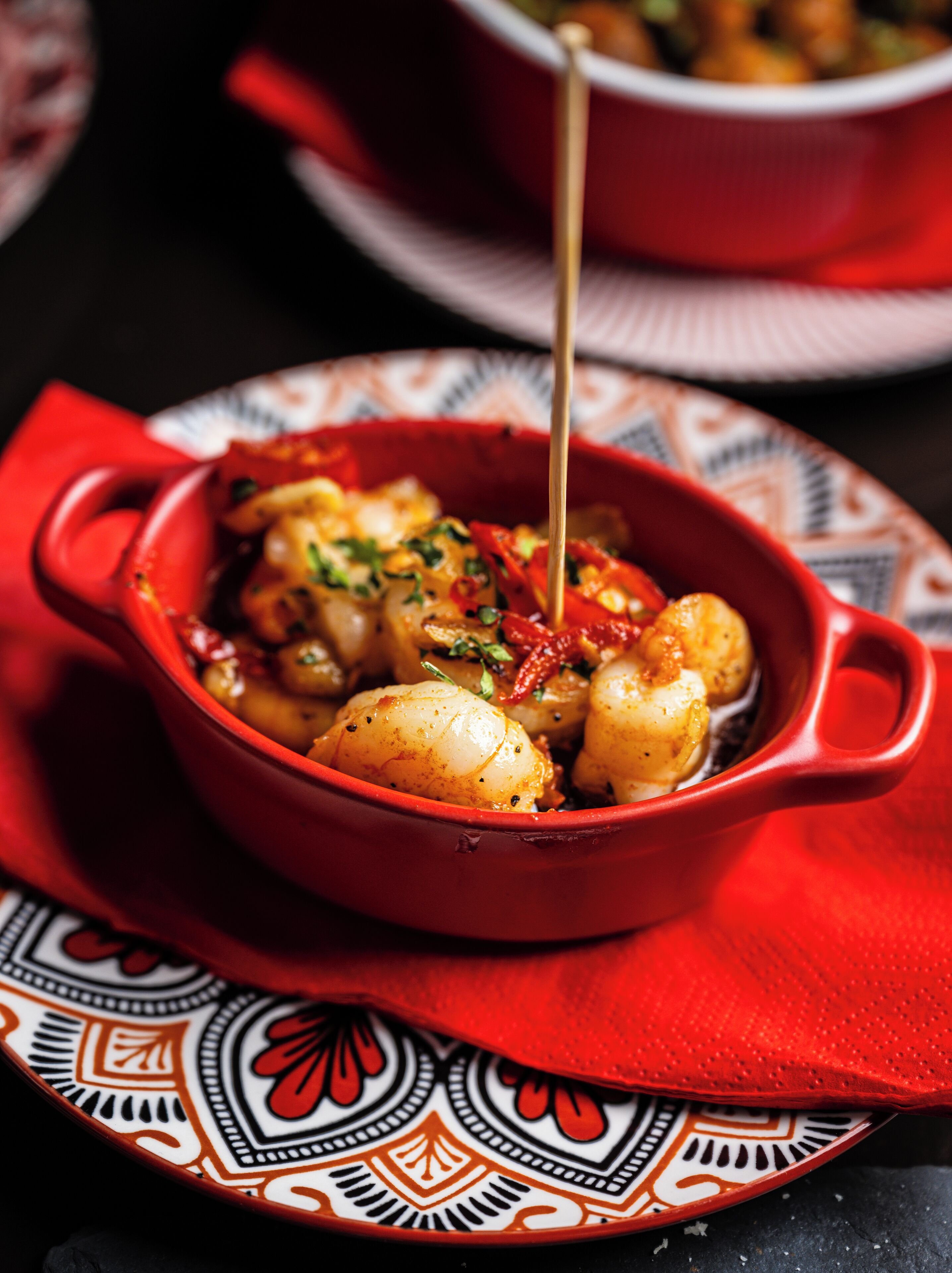 A red ceramic dish with food, placed on a patterned plate.