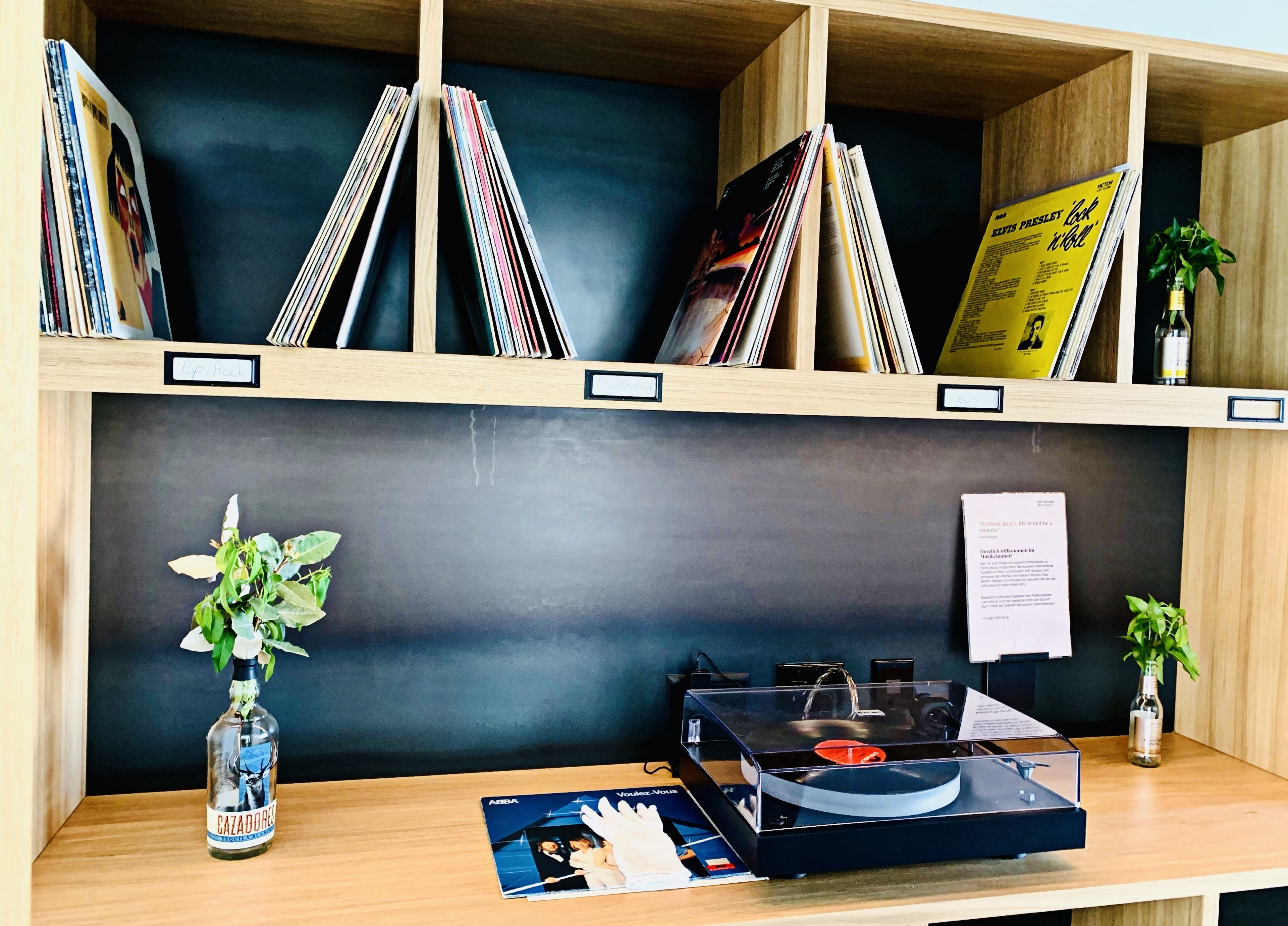 Una estant de fusta amb discos de vinil, un toca discs, una ampolla de licor i una petita planta.