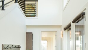 A spacious hallway with a staircase, a dining area in the background, and a glass door leading to a balcony.