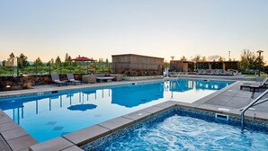 A swimming pool with lounge chairs and a covered area, surrounded by a landscaped garden and a building.