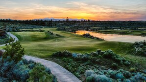 A golf course with a water body, a walking path, and a distant mountain range.