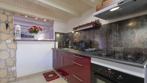 A compact kitchen with a stove, coffee maker, and a window with flowers.