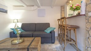 A cozy living room with a grey sofa, a wooden coffee table, and a stone wall with a mirror and bar stools.