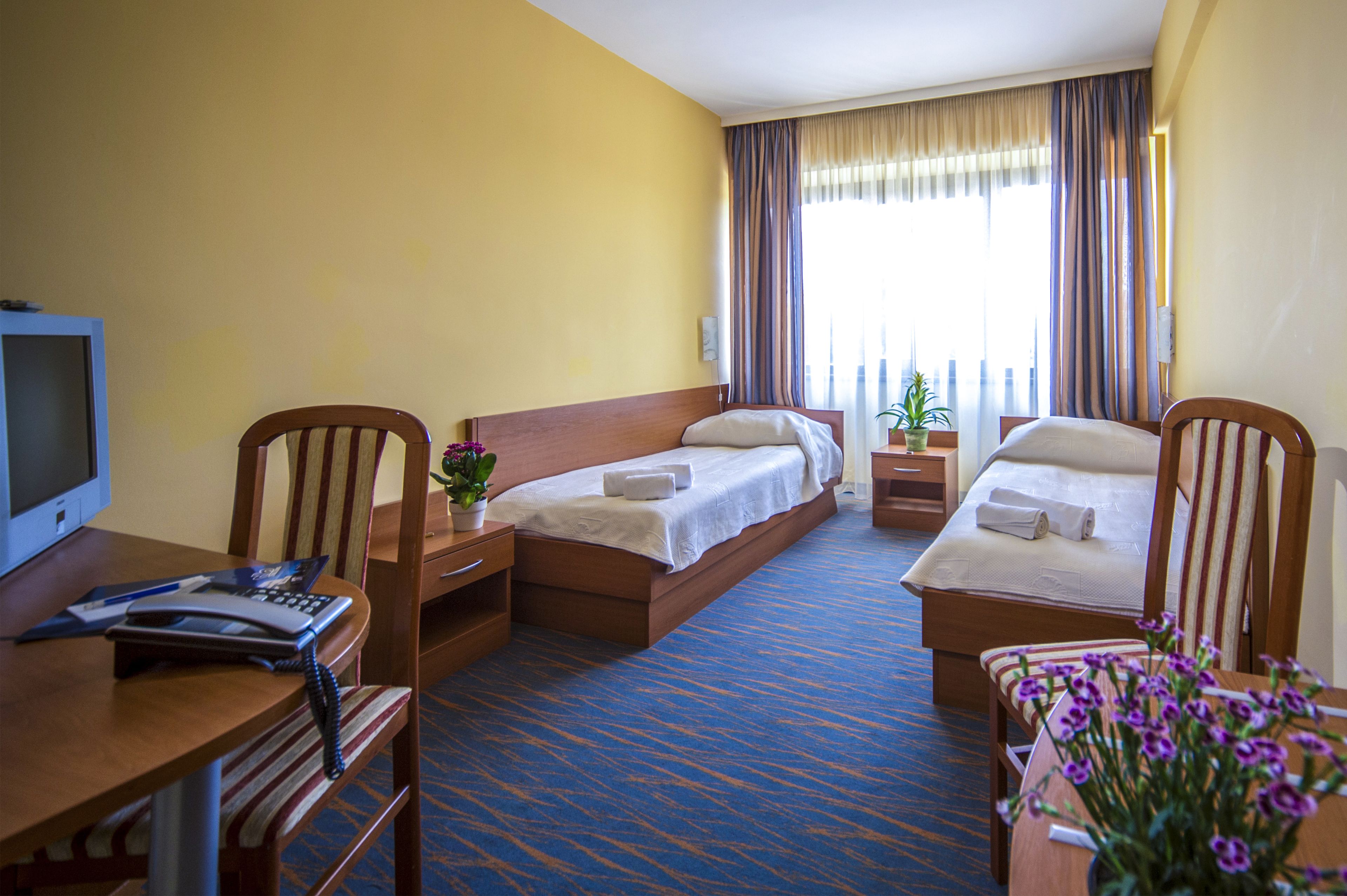 A hotel room with two beds, a desk with a computer, a telephone, and a small table with a plant.
