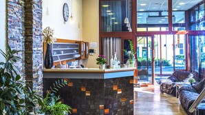 Un espace d’accueil avec un mur en briques, un comptoir d’accueil, des plantes en pot et un coin salon comprenant un canapé et des fauteuils.