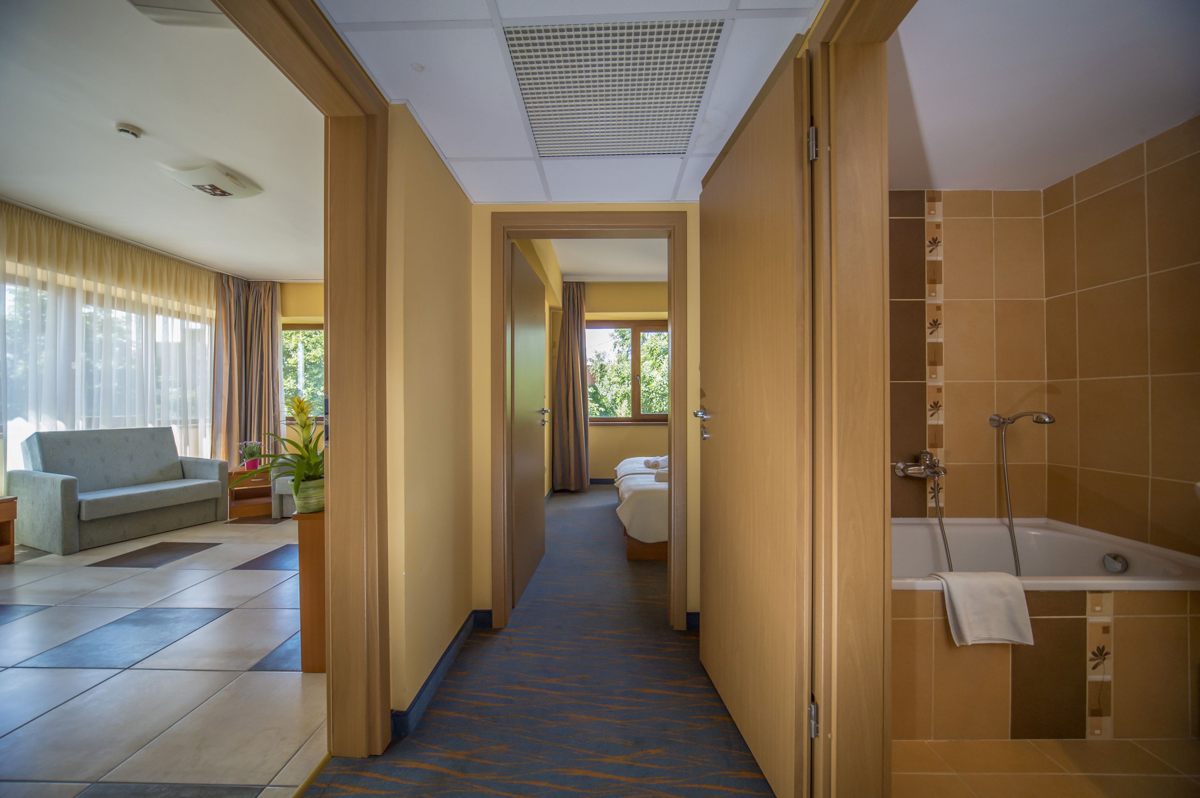 A hotel hallway with a sofa, a bed, and a bathroom with a bathtub.